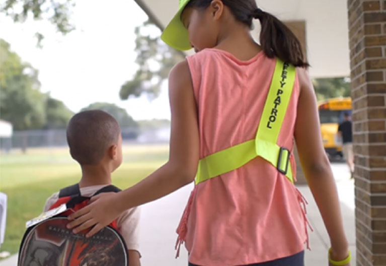 A safety patrol student helping child to bus.