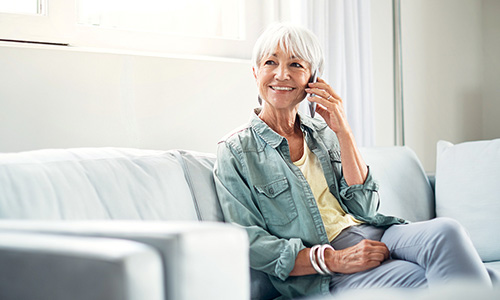 Elderly woman sitting on a couch talking on the phone.