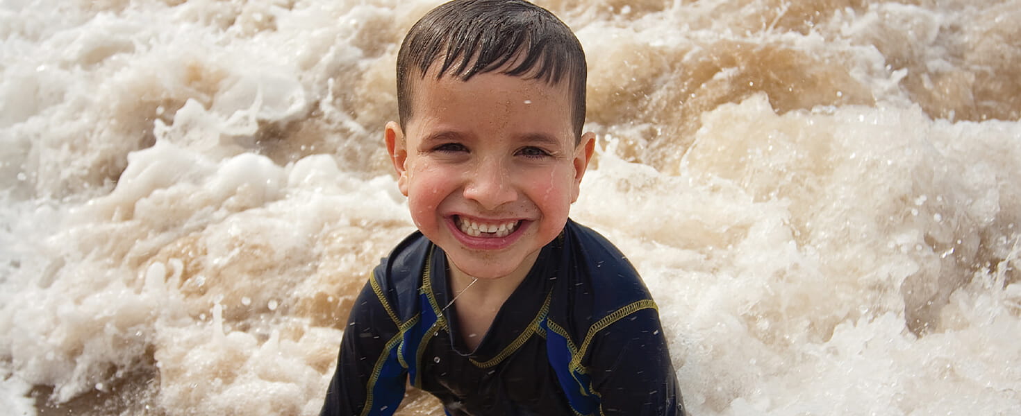 young child in wet suit playing in front of river