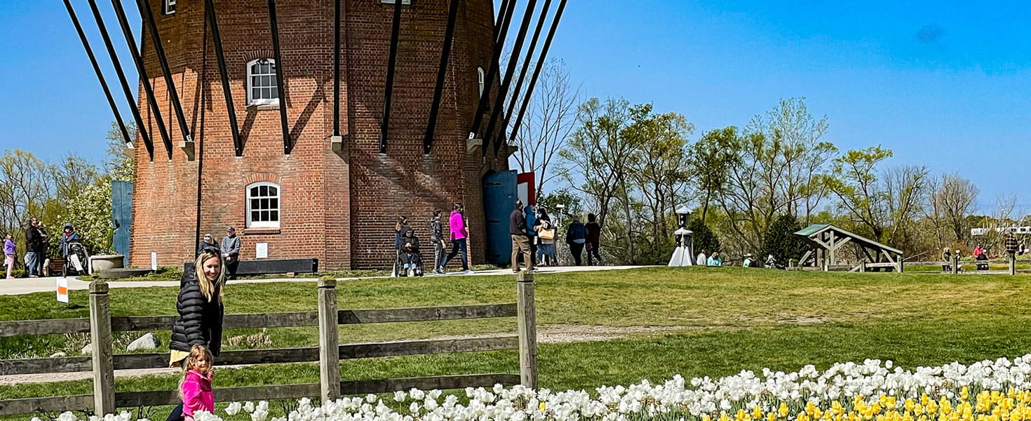 woman holds toddler's hand, walking in front of a lighthouse