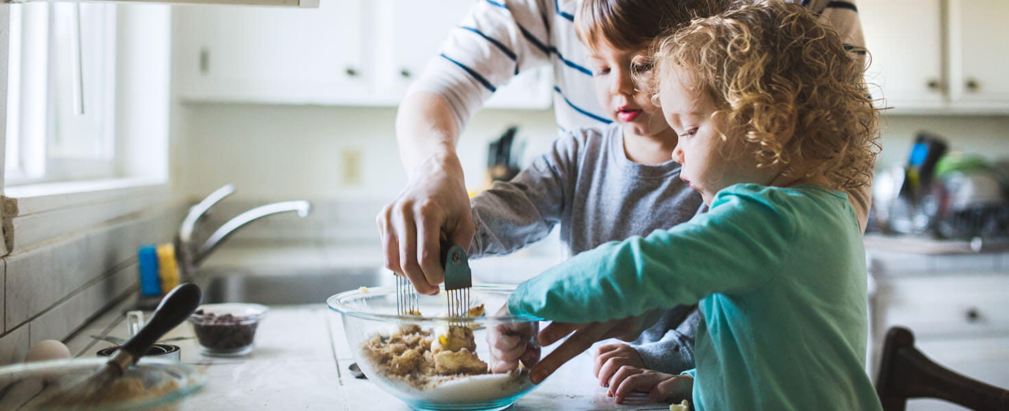 toddlers standing at kitchen counter making chocolate chip cookies