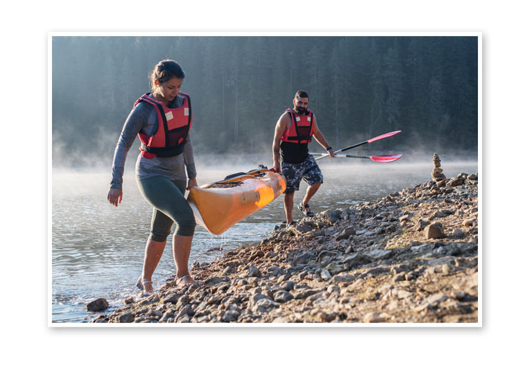 Man and woman carrying a kayak.