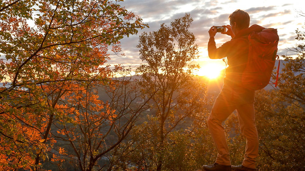 Person hiking up on a mountaintop vista taking a picture of the mountains