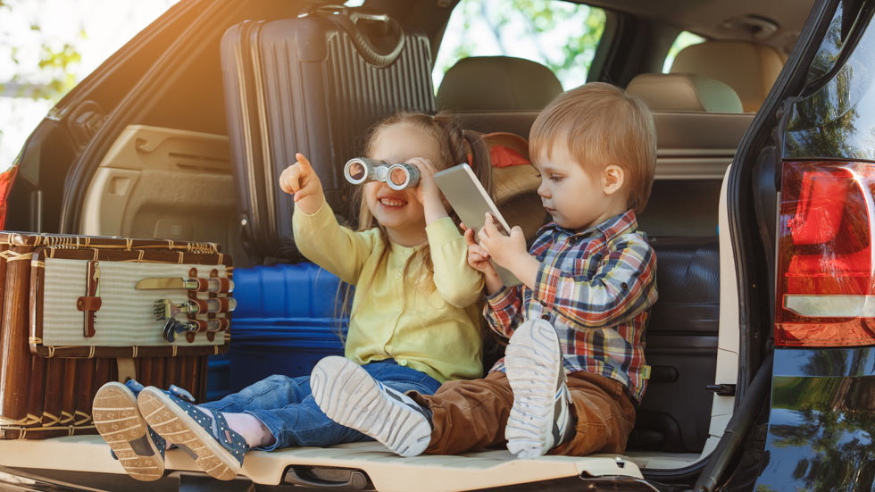 two toddlers sitting in the back of a parked car planning their adventure